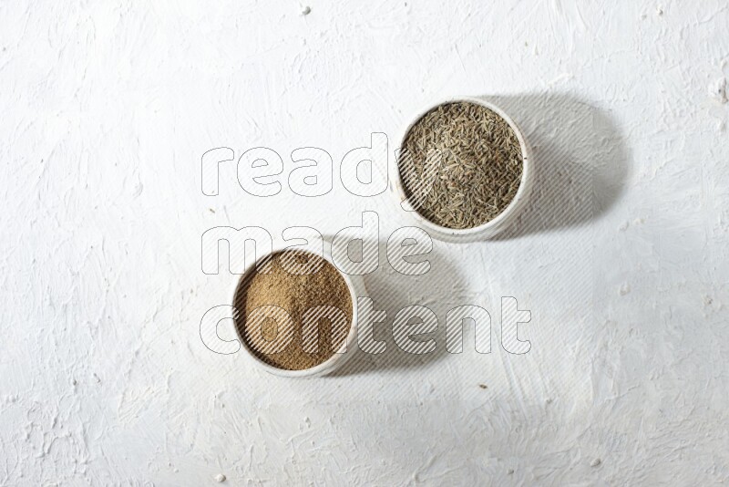 2 beige bowls full of cumin seeds and powder on a textured white flooring