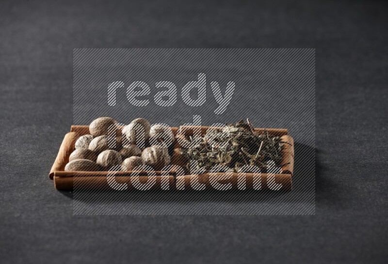 2 squares of cinnamon sticks full of nutmegs and dried basil on black flooring