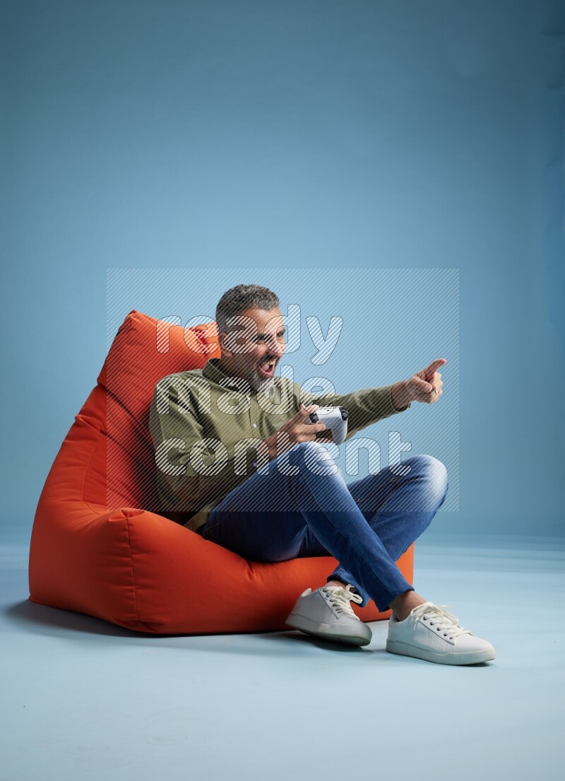 A man sitting on an orange beanbag and gaming with joystick