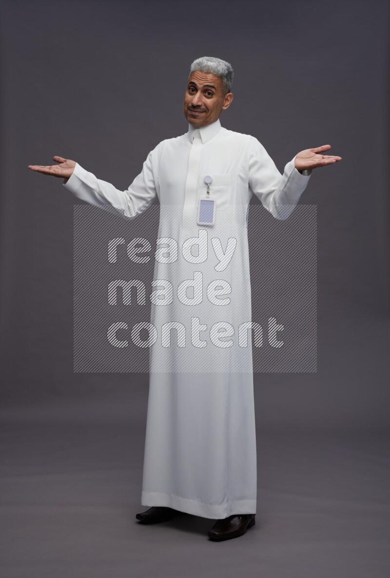 Saudi man wearing thob with pocket employee badge standing interacting with the camera on gray background
