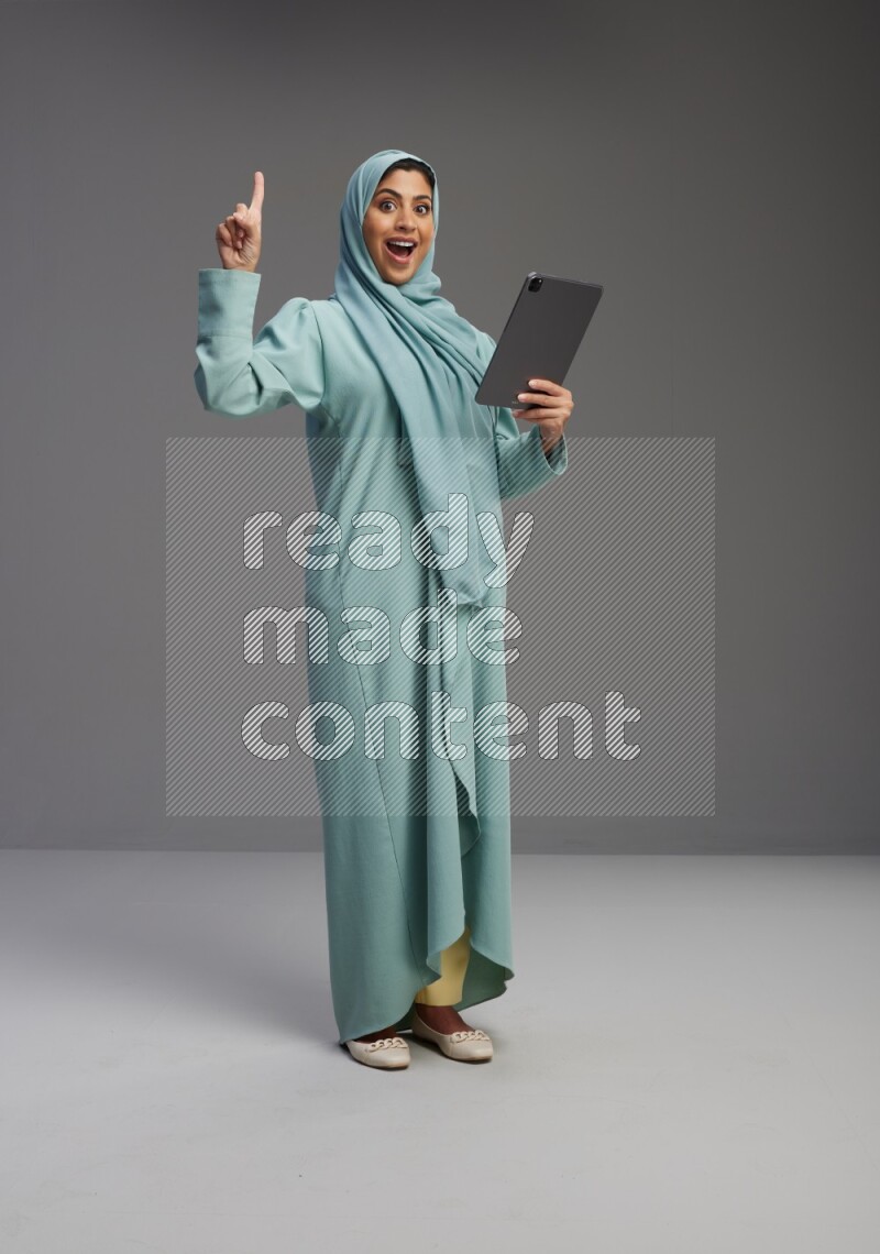 Saudi Woman wearing Abaya standing working on tablet on Gray background