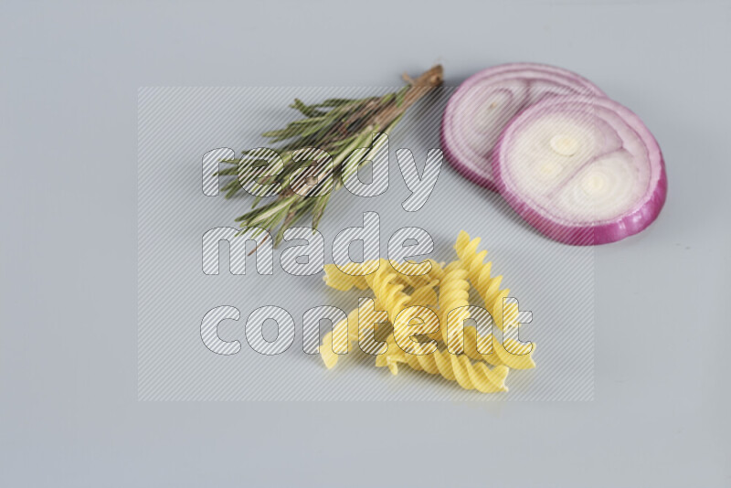 Raw pasta with different ingredients such as cherry tomatoes, garlic, onions, red chilis, black pepper, white pepper, bay laurel leaves, rosemary, cardamom and mushrooms on light blue background