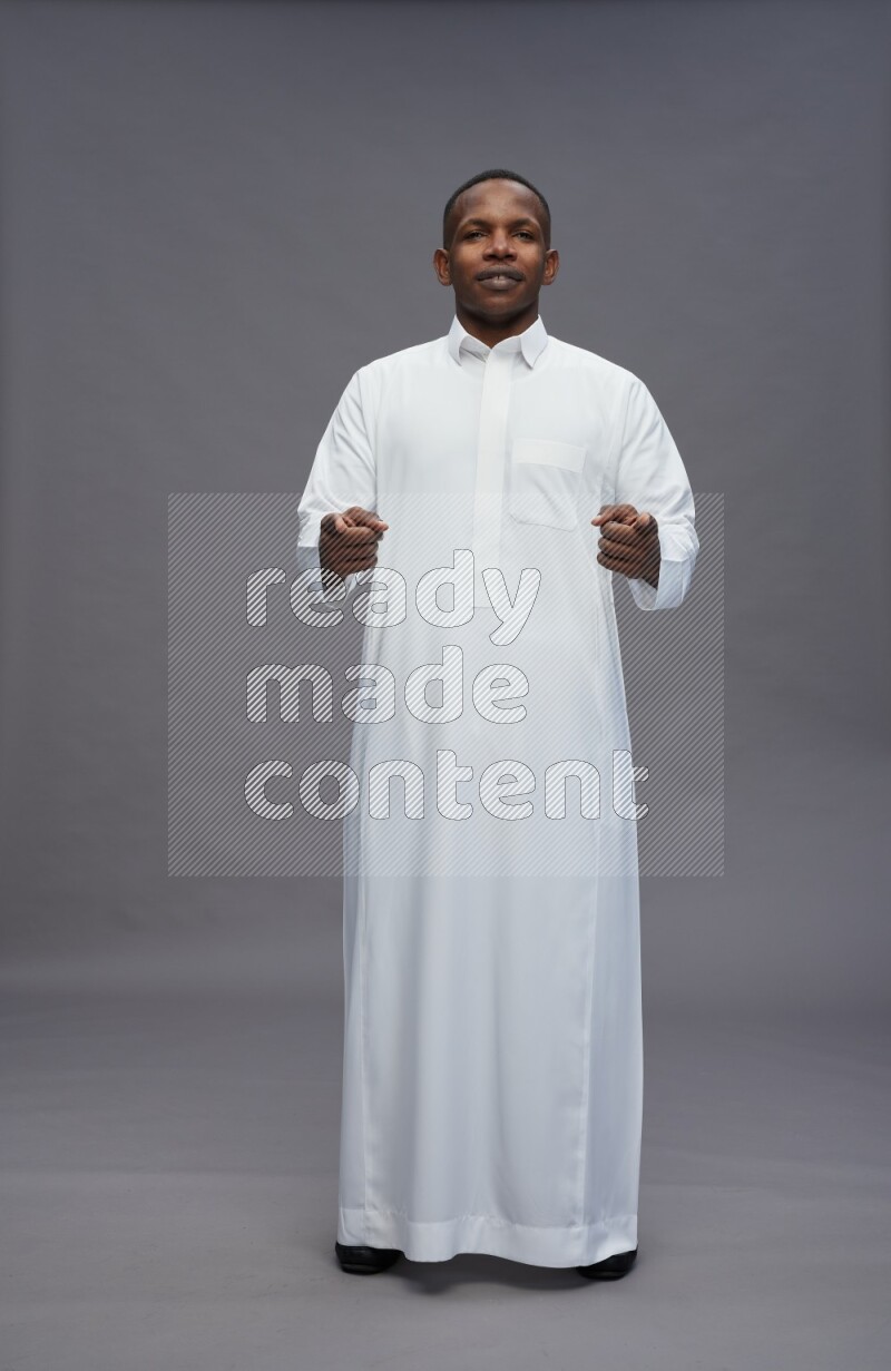 Saudi man wearing thob standing interacting with the camera on gray background