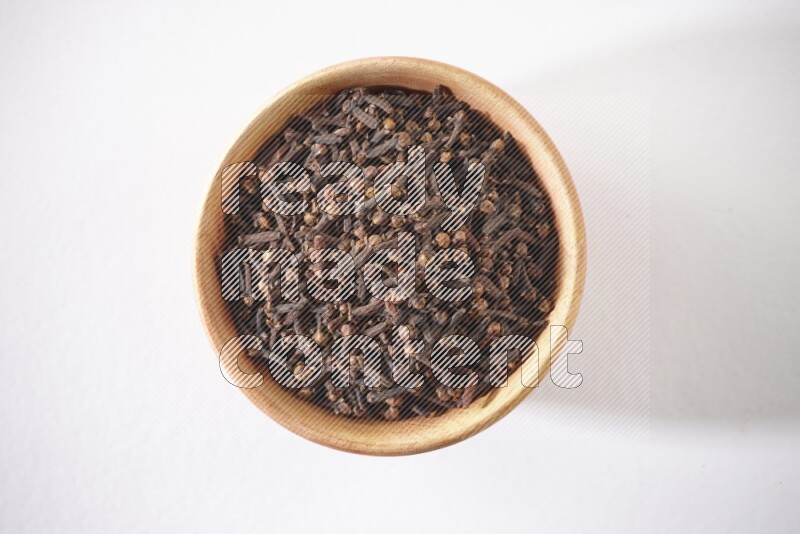 A wooden bowl full of cloves on a white flooring