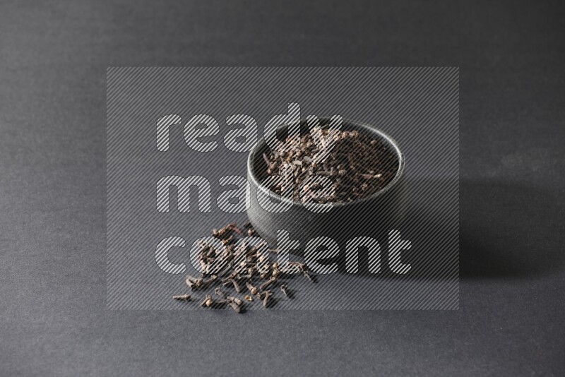 A black pottery bowl full of cloves on a black flooring