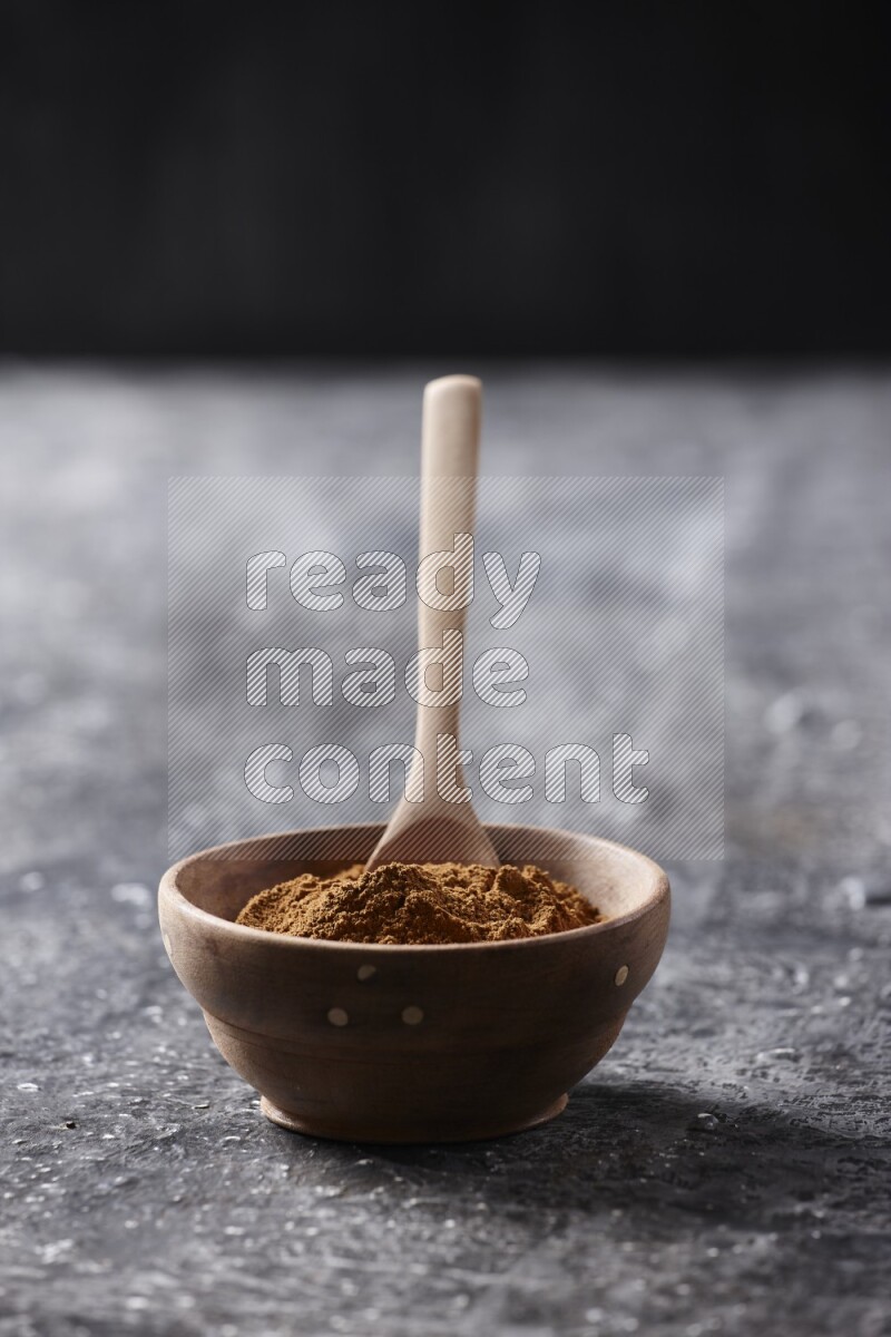Wooden bowl full of cinnamon powder with a wooden spoon on a textured black background in different angles