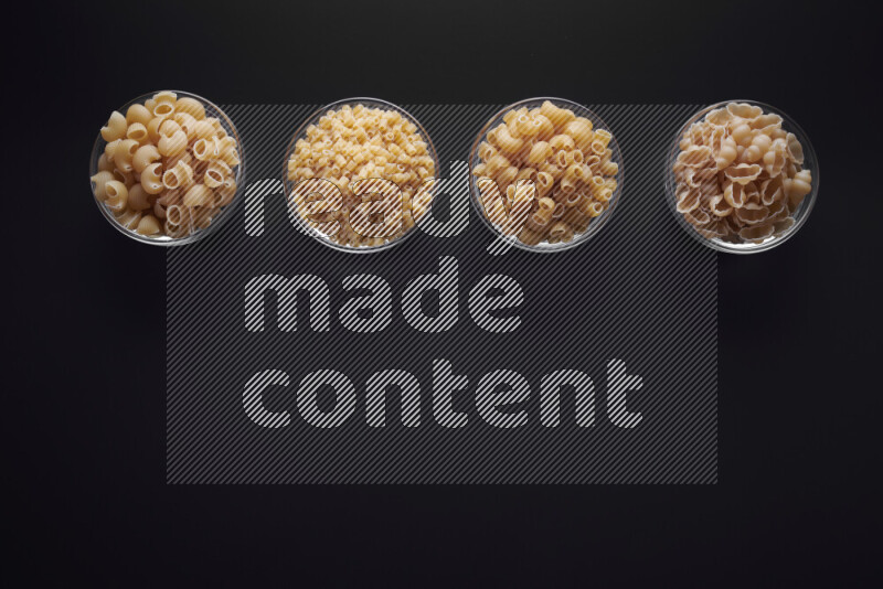 Different pasta types in glass bowls on black background