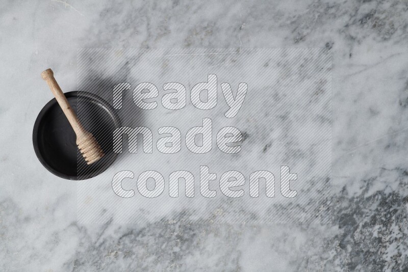 طبق فرن من الفخار الأسود مع ملعقة عسل خشبية بداخله على خلفية من الرخام الرمادي