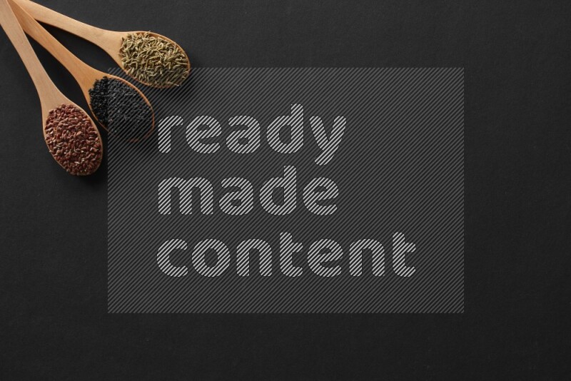 wooden spoons filled with white peppers, mustard seeds, black seeds, garden cress, cumin and flax on black flooring