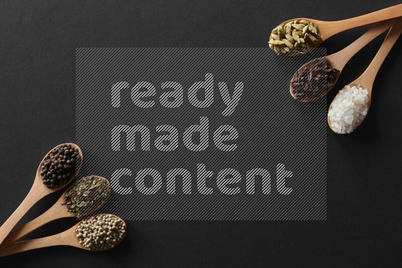 wooden spoons filled with white peppers, cloves, cardamom, salt, black peppers and basil on black flooring