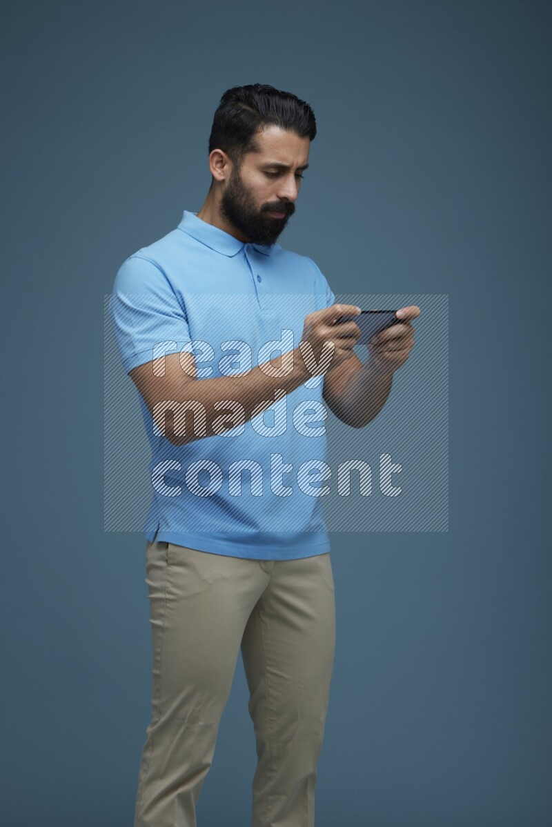 Man playing a game on his phone in a blue background wearing a Blue shirt