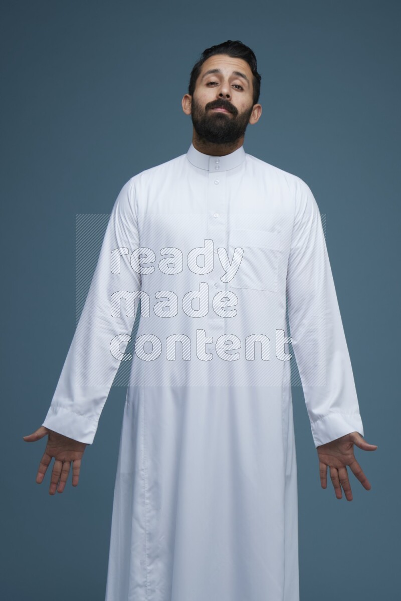 A man pointing in a blue background wearing Saudi Thob