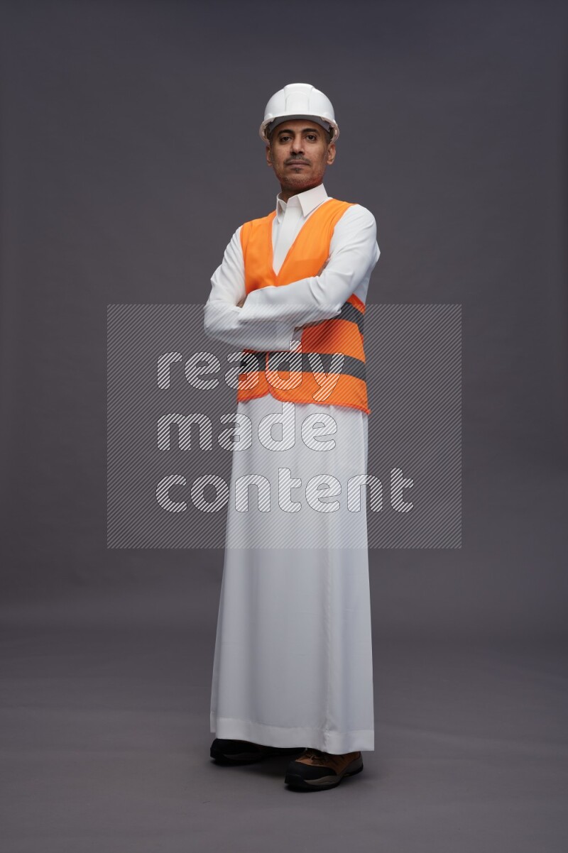 Saudi man wearing thob with engineer vest standing with crossed arms on gray background