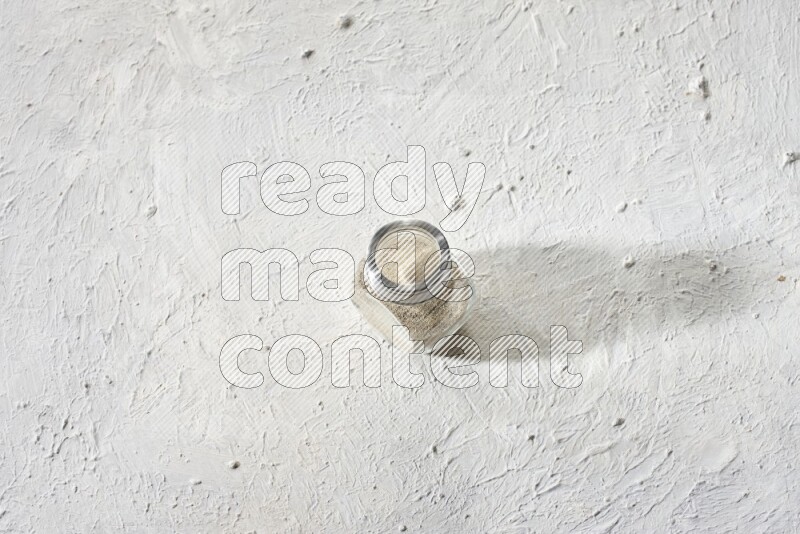 Herbal Glass jar full of white pepper powder on textured white flooring