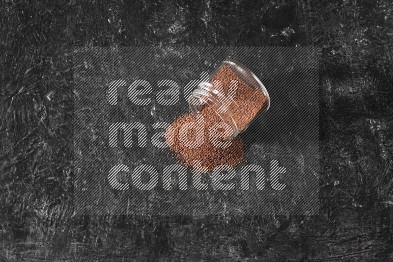 وعاء زجاجي مقلوب ممتلئ ببذور حب الرشاد وتناثرت البذور منه على أرضية سوداء