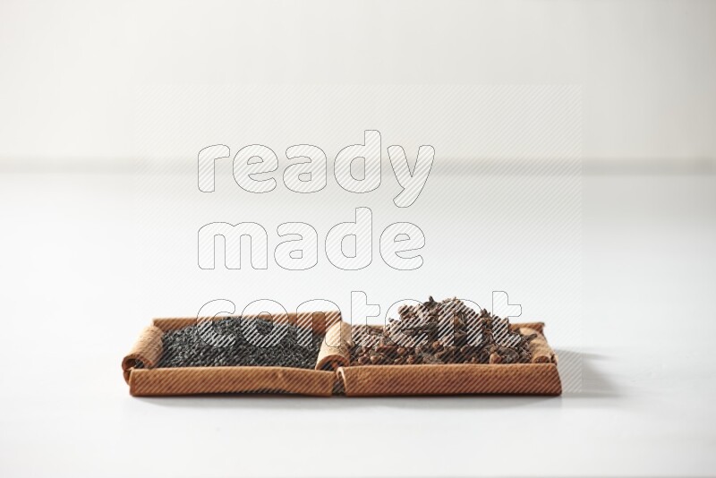 2 squares of cinnamon sticks full of cloves and black seeds on white flooring