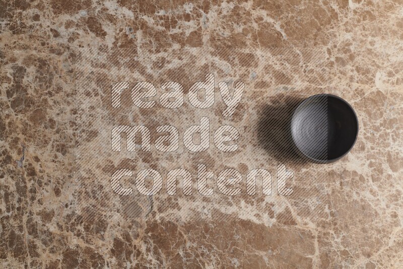 A black pottery bowl on beige marble background