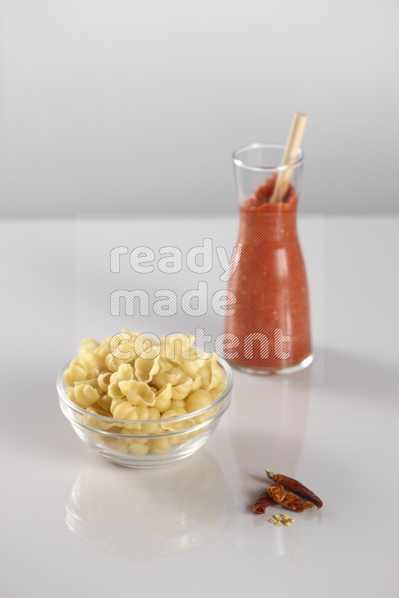 Raw pasta with tomatoe pasta with different ingredients such as cherry tomatoes, basil, garlic, bay laurel, cardamom, white pepper, black pepper, red chilis and wheat stalks on light grey background