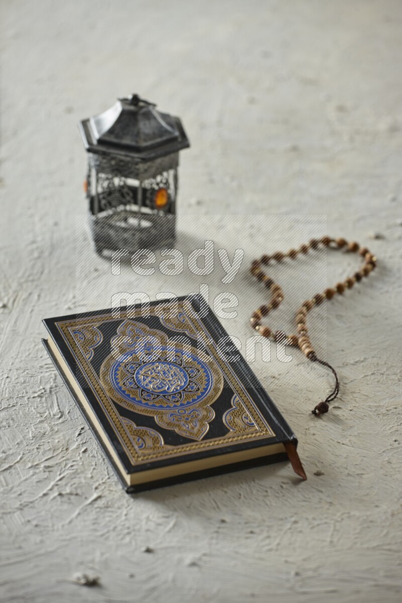 A silver lantern with different drinks, dates, nuts, prayer beads and quran on textured white background