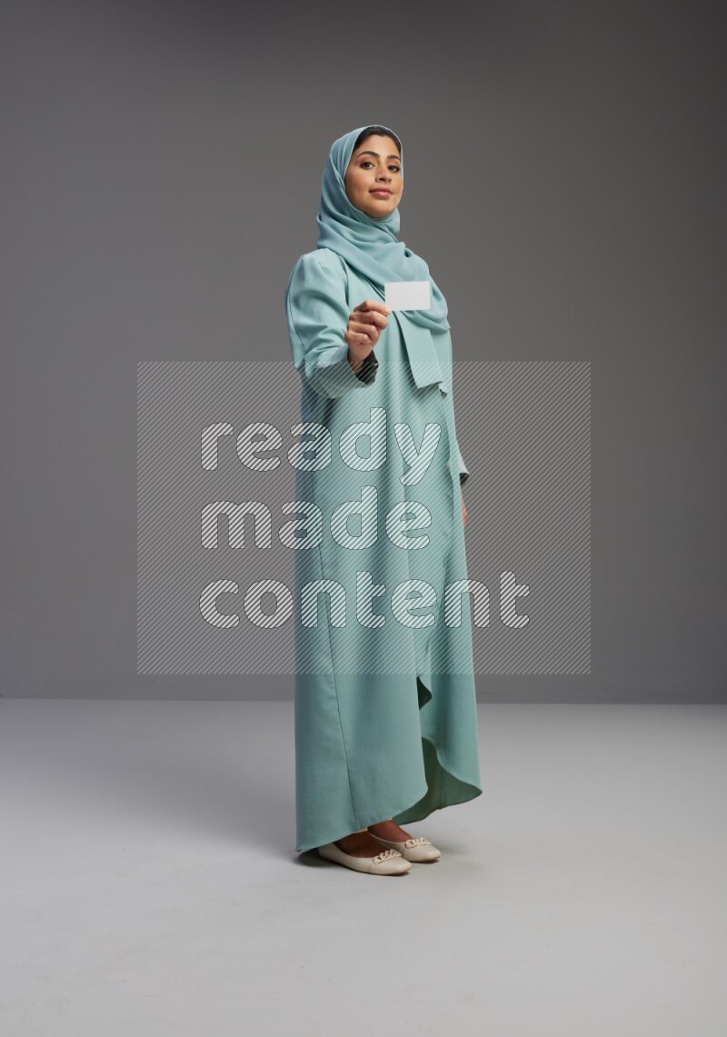Saudi Woman wearing Abaya standing holding ATM card on Gray background