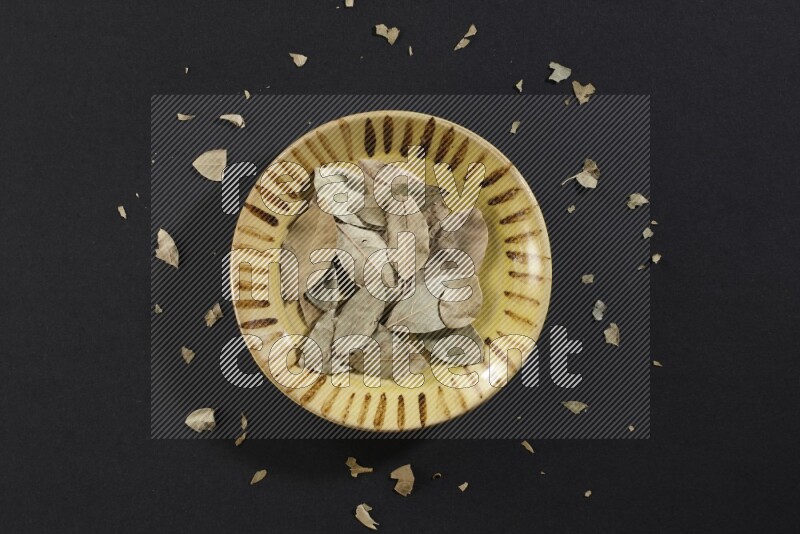 A multicolored pottery plate filled with dried bay leaves on black flooring