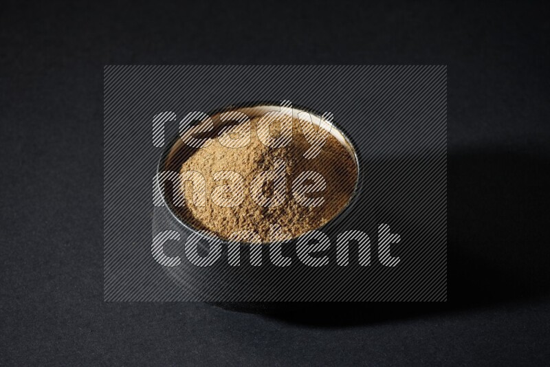 A black pottery bowl full of cumin powder on a black flooring