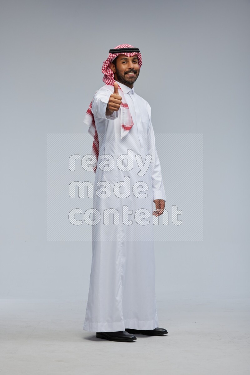 Saudi man Wearing Thob and shomag standing interacting with the camera on Gray background