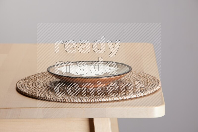 multi-colored pottery Plate placed on a big light colored straw placemat on the edge of wooden table