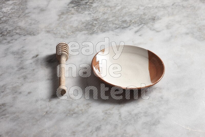 Multicolored pottery plate with wooden honey dipper on the side on grey marble background