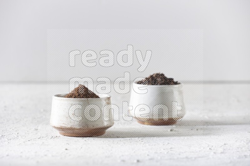 2 Beige ceramic bowls, one full of cloves and the other full of powder on textured white flooring