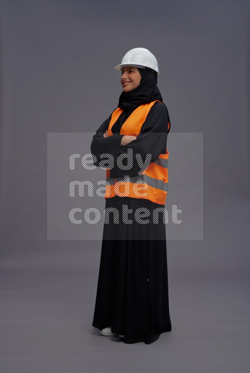 Saudi woman wearing Abaya with engineer vest standing with crossed arms on gray background