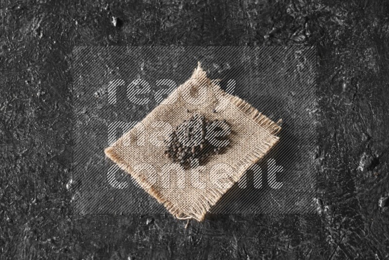 Black pepper on burlap fabric on a textured black flooring