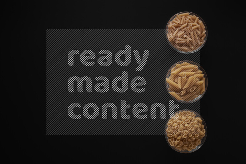 Different pasta types in 3 glass bowls on black background
