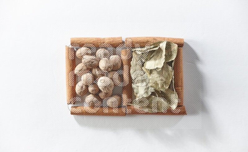 مربعان من أعواد القرفة ممتلئان بأوراق الغار وجوزة الطيب علي خلفية بيضاء