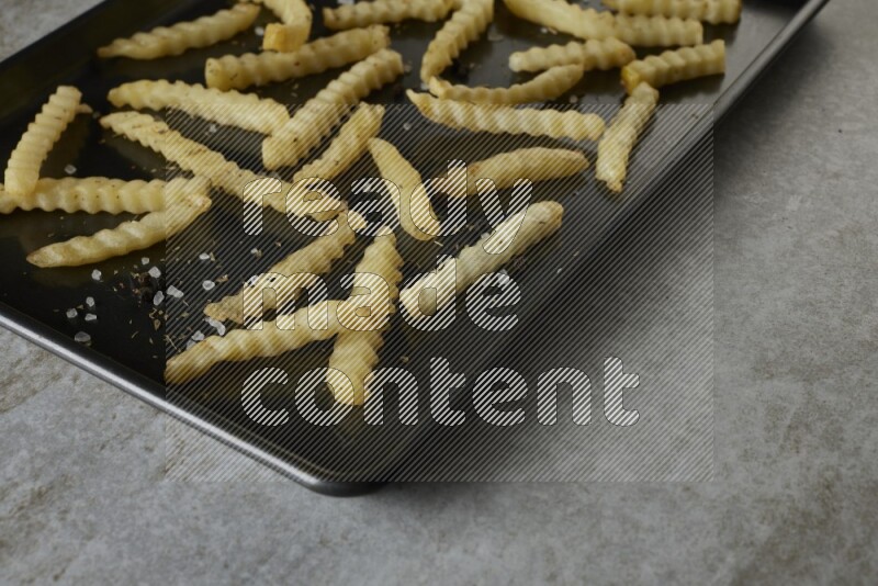 crinkle fries in a black stainless steel rectangle tray on grey textured counter top