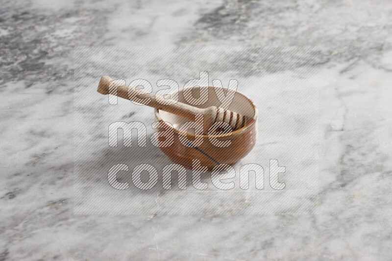 Multicolored pottery bowl with wooden honey dipper in it on grey marble background