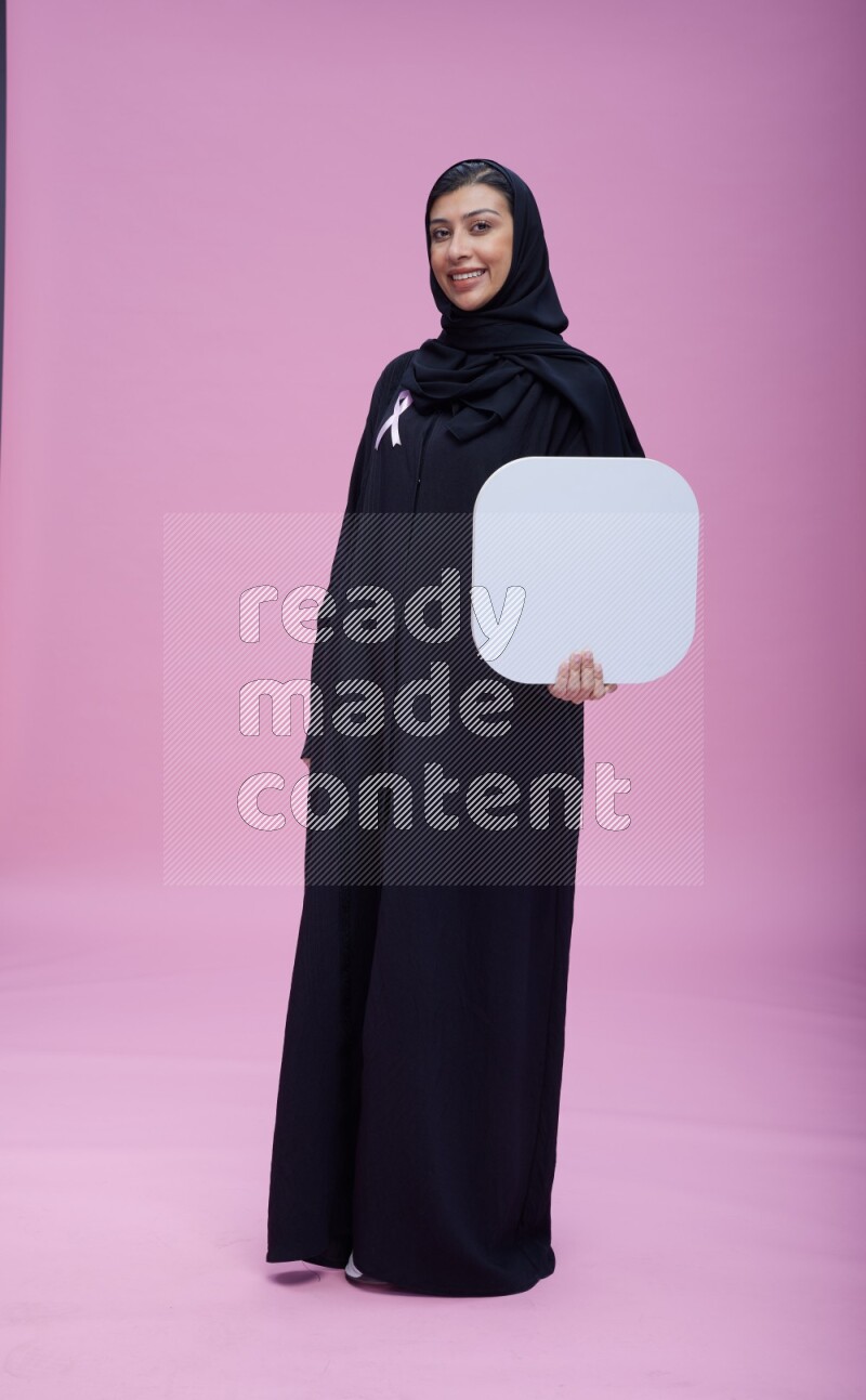 Saudi woman wearing pink ribbon on Abaya standing holding social media signs on pink background