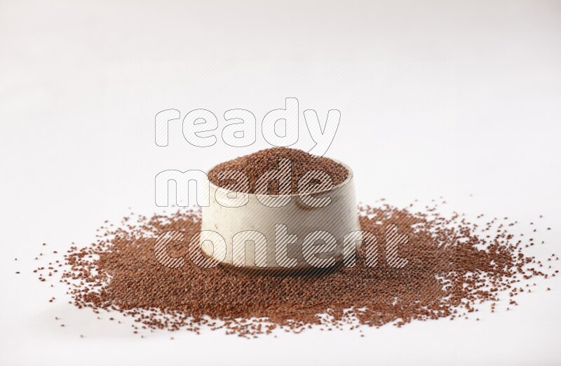 A beige pottery bowl full of garden cress seeds with more seeds spread on a white flooring