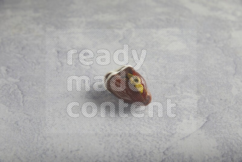 pistachio stuffed date covered with dark chocolate with white chocolate drizzle on a light grey background