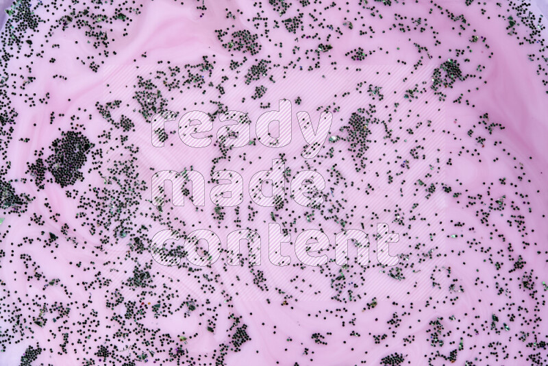 A close-up of sparkling green glitter scattered on swirling pink background