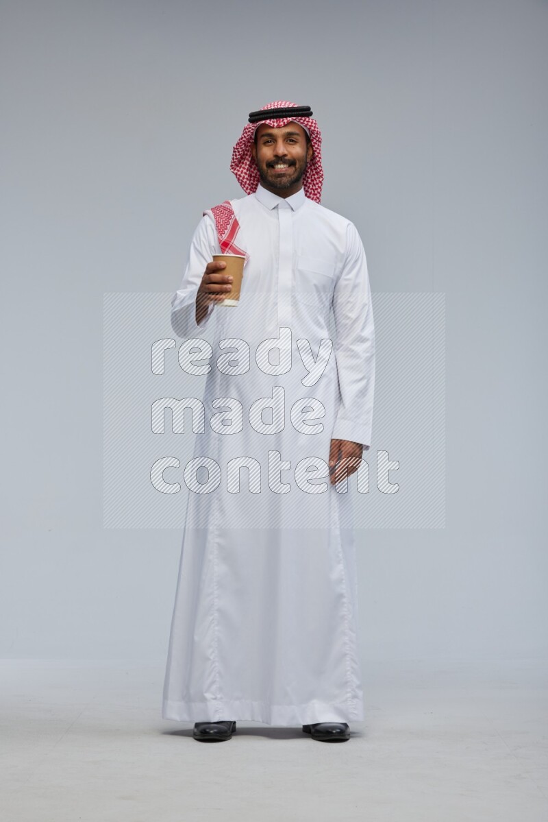 Saudi man Wearing Thob and shomag standing holding paper cup on Gray background