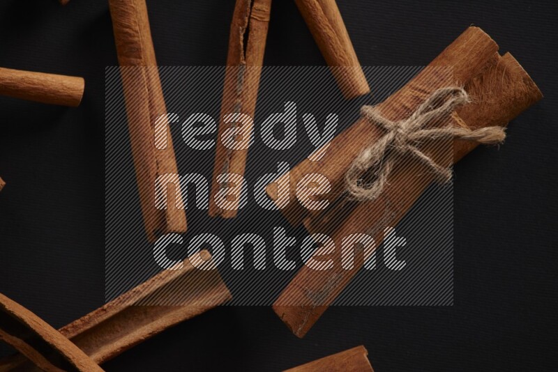 4 Cinnamon sticks stacked and bounded with more sticks in the background on black flooring