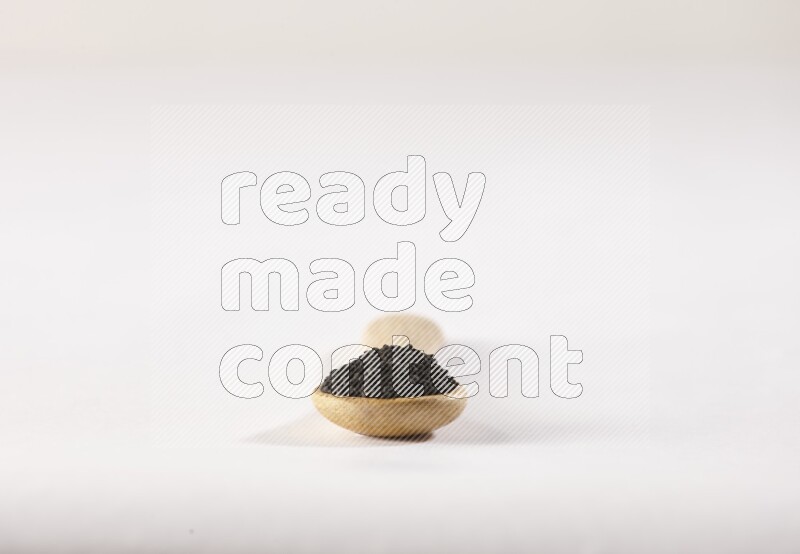 A wooden spoon full of black seeds on a white flooring
