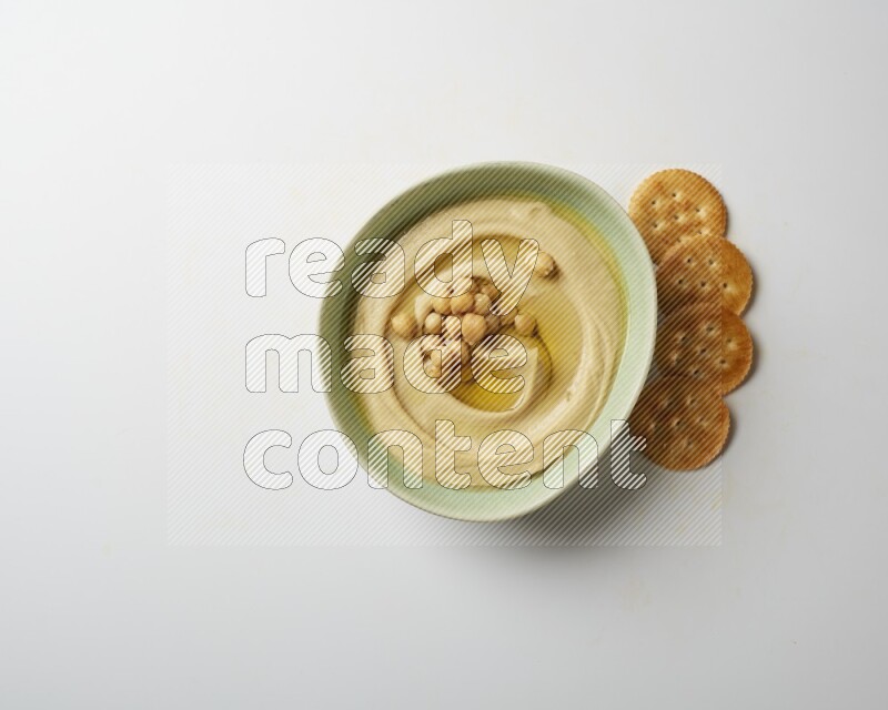 Hummus in a green plate garnished with roasted chickpeas  on a white background