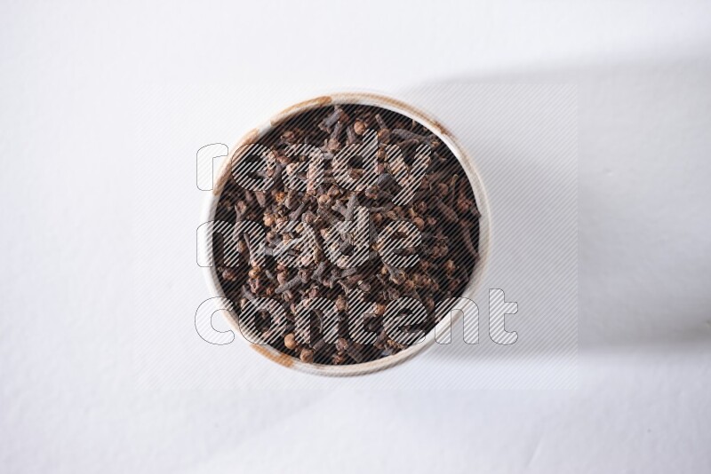 A beige ceramic bowl full of cloves on a white flooring