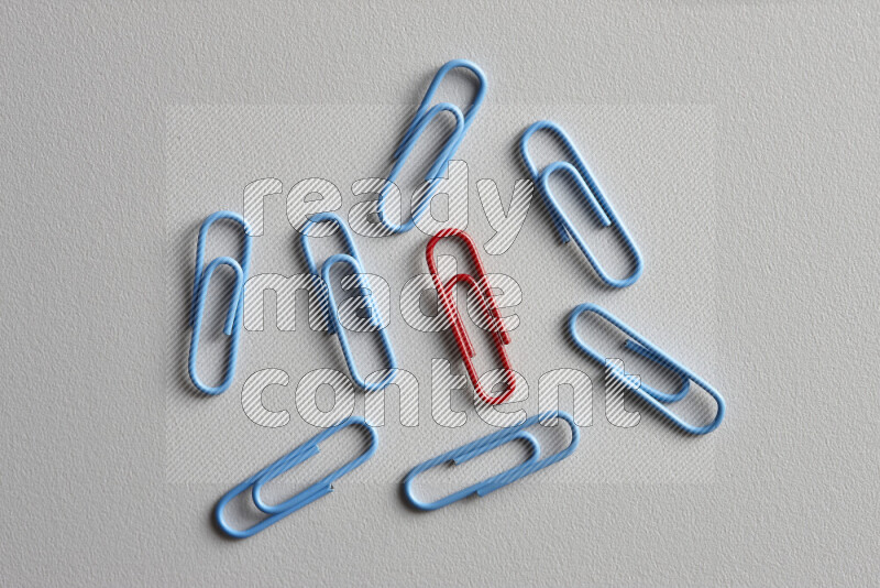 A bunch of blue paper clips with a different colored paper clip in the center on grey background