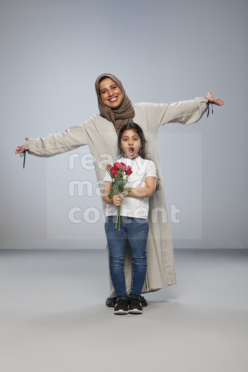 A girl standing giving flowers to her mother on gray background