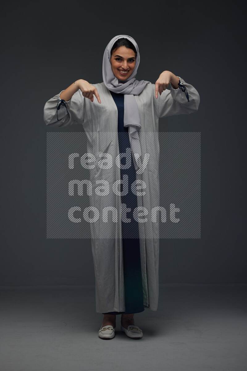 A Saudi woman wearing a light gray Abaya and head scarf standing and making multi poses eye level on a grey background