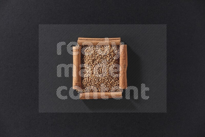 A single square of cinnamon sticks full of mustard seeds on black flooring