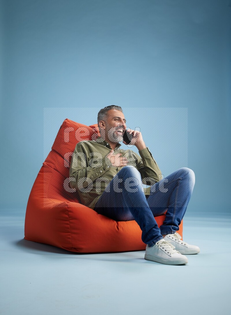 A man sitting on an orange beanbag and talking on the phone